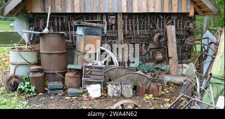 Barili e taniche di utensili arrugginiti gettati vicino a un capannone di legno Foto Stock