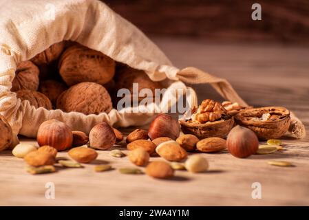 Noci di mandorle, nocciole, noci e semi dolci in un sacchetto di burlap su uno sfondo di legno. Foto Stock