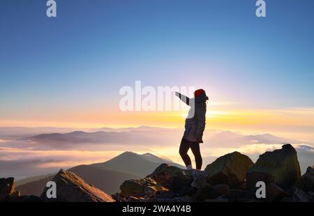 Ragazza con la mano sollevata sulla cima della montagna alla bella alba mattutina. Foto Stock