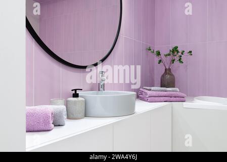 Gli interni del bagno sono in stile minimalista con piastrelle rosa, specchio rotondo sopra il lavandino e gli asciugamani. Foto Stock