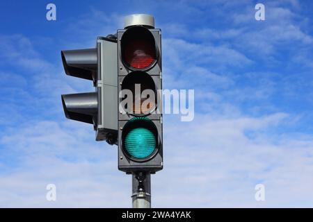 Semaforo verde contro cielo blu e nuvole bianche. Foto Stock