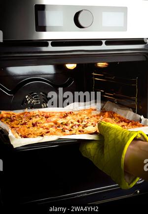 Un uomo tira fuori la pizza dal forno in un guanto per preparare le lenzuola. Pizza fatta in casa. Foto Stock