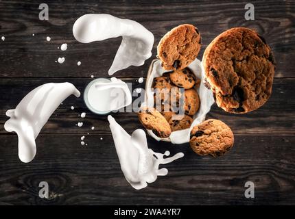 Bicchiere di latte con gustosi biscotti in un cestino. Vista dall'alto. Spruzzi di latte e biscotti volanti. Sfondo sfocato del vecchio tavolo in legno. Rustico e polveroso Foto Stock