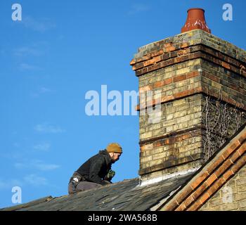 Workman sul tetto della casa che fa le riparazioni e Chimney vittoriano. Foto Stock