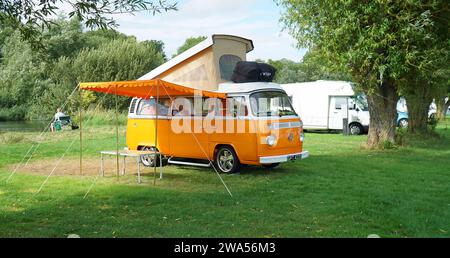Classic Orange Volkswagen Camper Van parcheggiato sul campo Site dal fiume con il rabbocco e la tenda . Foto Stock