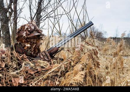 Un cacciatore di anatre mimetizzato siede in un nascondiglio mascherato. Ha in mano un fucile. Foto Stock