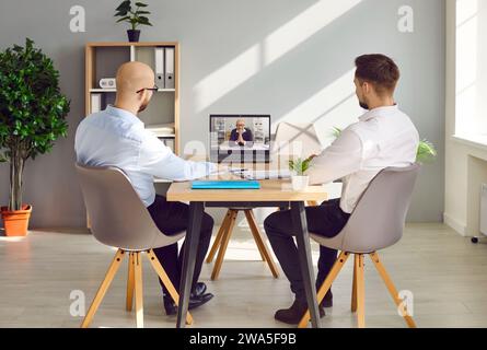 Vista posteriore di due uomini d'affari che parlano con i colleghi durante la videoconferenza Foto Stock