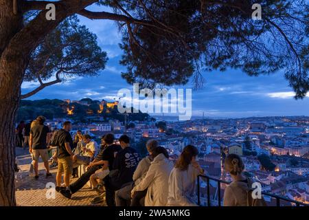 Lisbona, Portogallo - 15 ottobre 2023 - la gente si rilassa al punto panoramico di Miradouro da Graca la sera, con vista della capitale da una collina. Foto Stock