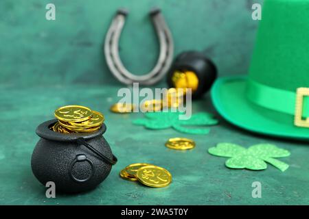 Pentole di monete d'oro e trifoglio di carta con cappello a leprechaun e ferro di cavallo su sfondo verde grunge. St Festa del giorno di Patrick Foto Stock