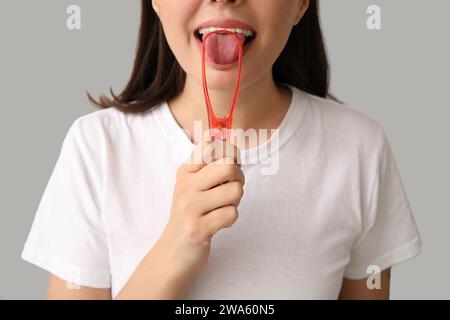 Giovane donna che usa il raschietto della lingua su sfondo chiaro, primo piano Foto Stock