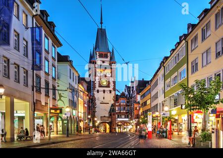 Scena notturna lungo Kaiser-Joseph-Straße con Martinstor, una delle due porte rimanenti dalla città medievale di Friburgo in Brisgovia, Germania. Foto Stock