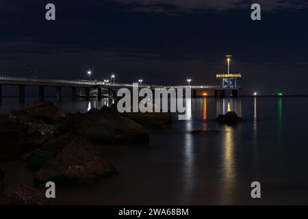 Vista notturna del molo sul mare, splendidi riflessi di luce colorata nell'acqua - Burgas, Bulgaria Foto Stock