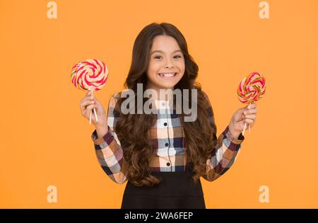 I lecca-lecca rendono la bocca felice. Le bambine si divertono durante le vacanze scolastiche. I bambini piccoli e felici mangiano lecca lecca-lecca. Grandi lecca-lecca-lecca a vortice sui bastoncini. S Foto Stock