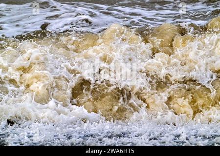 Onde che si infrangono/rotolano su una spiaggia sabbiosa che mostra acque marroni e torbide con sabbia durante la tempesta invernale lungo la costa del Mare del Nord in Zelanda, Paesi Bassi Foto Stock