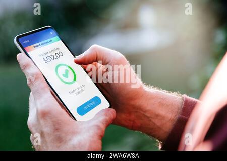 Uomo che effettua trasferimenti di denaro online utilizzando app per inviare e ricevere valuta. Telefono cellulare con un'applicazione finanziaria sullo schermo. Concetto di trasferimento di denaro Foto Stock