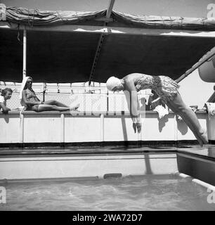 1953, storica, una giovane donna in vacanza a Ceylon (Sri Lanka), in costume da bagno dell'epoca e cappello da bagno, tuffandosi in una piscina all'aperto all'aperto su una barca. Situata nell'Oceano Indiano nell'Asia meridionale, l'isola divenne una Repubblica Democratica Socialista nel 1972 e cambiò il suo nome in Sri Lanka. Foto Stock