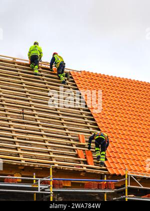 Tre lavoratori che indossano indumenti da lavoro protettivi installano nuove tegole di argilla, nuovi strati di piastrelle di argilla Foto Stock