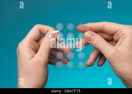 Primo piano cerotto acne rotondo sul dito su sfondo blu. Macchie di acne per il trattamento del brufolo e della rosacea da vicino. Pulizia viso ringiovanente cosme Foto Stock