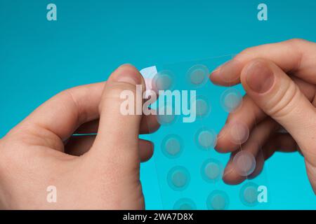 Primo piano cerotto acne rotondo sul dito su sfondo blu. Macchie di acne per il trattamento del brufolo e della rosacea da vicino. Pulizia viso ringiovanente cosme Foto Stock