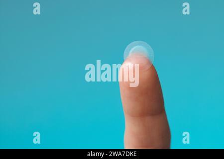 Primo piano cerotto acne rotondo sul dito su sfondo blu. Macchie di acne per il trattamento del brufolo e della rosacea da vicino. Pulizia viso ringiovanente cosme Foto Stock