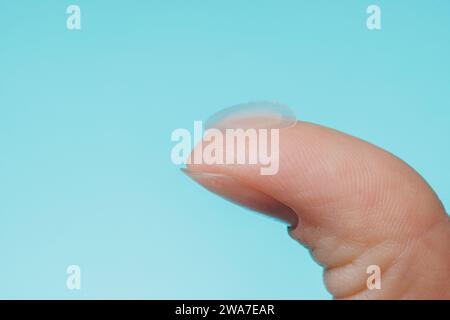 Primo piano cerotto acne rotondo sul dito su sfondo blu. Macchie di acne per il trattamento del brufolo e della rosacea da vicino. Pulizia viso ringiovanente cosme Foto Stock