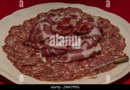 Salame a fette e soppressata disposti su piatto bianco sopra la tovaglia rossa Foto Stock