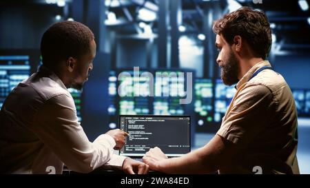 Team di sviluppatori IT che scrive codice script server nel data center sul terminale laptop. Programmatori di lavoro di squadra che eseguono lavori di manutenzione in impianti ad alta tecnologia aggiornando il software dei carri di perforazione Foto Stock