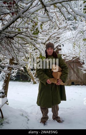 Uomo che porta legna da ardere attraverso la caduta di neve in giardino per uso come combustibile in un bruciatore di legno Zala county Ungheria Foto Stock