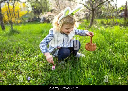 Gilr con le uova da pittura. La bambina carina indossa le orecchie del coniglio. Concetto di caccia pasquale Foto Stock