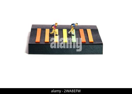 Fotografia creativa di figure giocattolo per persone in miniatura. Installazione delle note adesive. Ragazzi studenti che camminano a zebra attraversando la strada. Isolato su bac bianco Foto Stock
