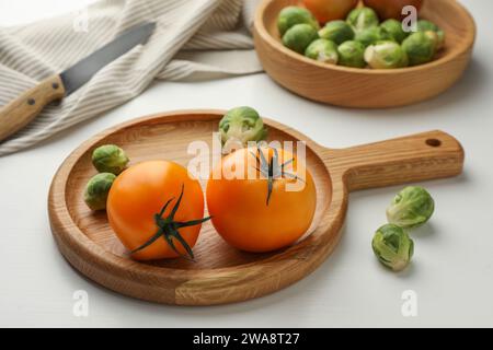 Tagliere con cavoletti di Bruxelles e pomodori su tavola di legno bianco Foto Stock