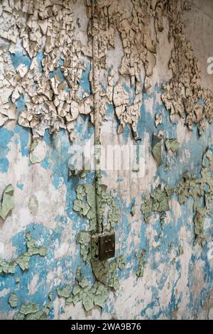 Un muro di vernice blu chiaro e verde screpolata e arricciata sopra l'intonaco ha una piccola scatola di interruttori elettrici all'Eastern State Penitentiary, in Pennsylvania. Foto Stock