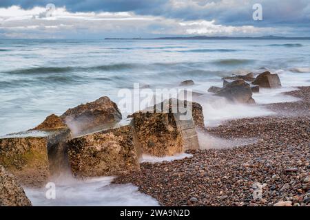 Blocchi di cemento anticarro resistenti agli agenti atmosferici nel mare ventoso. Findhorn Beach, Morayshire, Scozia. Esposizione lunga Foto Stock