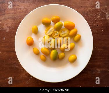 Frutta kumquat in piatto bianco su sfondo di legno Foto Stock