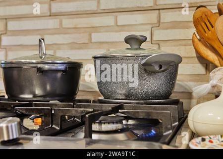 Cucina vivace con pentole e coperchi diversi su una stufa a gas, fiamme che bruciano, mentre il cibo delizioso viene preparato a casa, creando un ambiente accogliente e accogliente Foto Stock