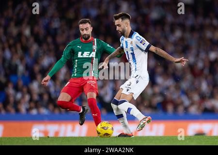 Brais Mendez della Real Sociedad compete per il pallone con Abde Rebbach del Deportivo Alaves durante la partita di calcio del campionato spagnolo la Liga tra Real Sociedad e Deportivo Alaves il 2 gennaio 2024 alla reale Arena di San Sebastian, in Spagna Foto Stock