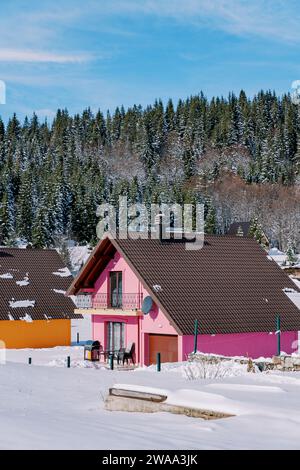 Casa rosa a due piani con terrazza sulla neve ai margini di una foresta di conifere nel villaggio Foto Stock