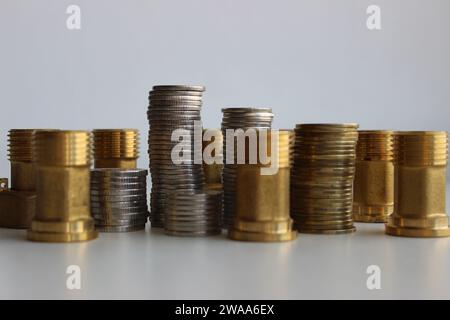 Raccordi in ottone e pile di monete in argento e ottone in colonne isolate su bianco Foto Stock
