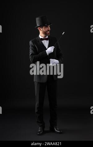 Felice mago che tiene la bacchetta su sfondo nero Foto Stock