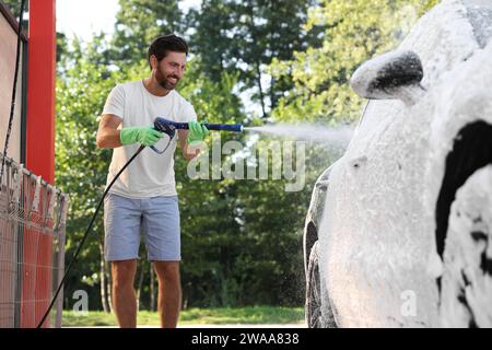 Uomo che copre l'automobile con schiuma all'autolavaggio esterno Foto Stock