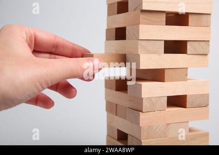 Donna che gioca a Jenga su sfondo grigio chiaro, primo piano Foto Stock