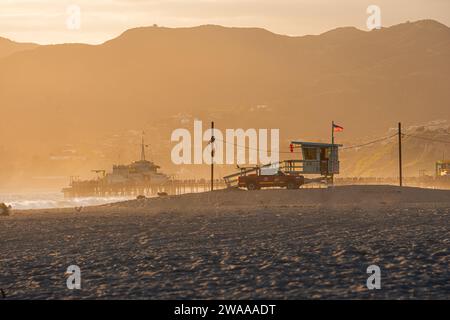 Torre del bagnino a Santa Monica al tramonto a maggio, sabbia bianca e condizioni di nebbia. Silhouette di un bagnino. Bandiera americana Foto Stock