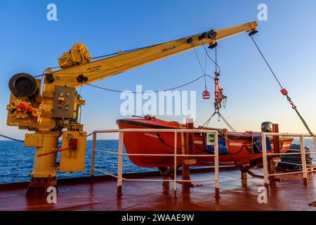 Nave di salvataggio arancione su una grande nave da carico e gru. Trapano uomo a bordo. Addestramento in scialuppa di salvataggio. Foto Stock