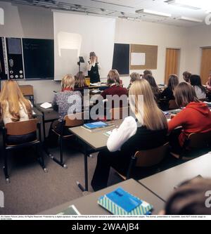 Negli anni '1970 Una classe scolastica siede sulle panchine durante una lezione con un'insegnante donna. Nella parte anteriore è presente un proiettore, un dispositivo comune nelle aule dell'epoca che mostrava il foglio trasparente con testo e immagini posizionati sullo schermo del dispositivo. I proiettori a soffitto erano ampiamente utilizzati nell'istruzione e nelle imprese prima dell'avvento della proiezione computerizzata. Svezia 1970 Foto Stock