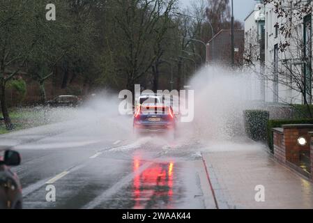 Lubeck, Germania. 03 gennaio 2024, Schleswig-Holstein, Lübeck: Un'auto attraversa una grande pozzanghera su una strada dell'Obertrave. La città anseatica di Lübeck ha avvertito del pericolo di inondazioni in alcune parti del centro città mercoledì. Secondo le previsioni, il livello dell'acqua dovrebbe raggiungere un'altezza di 1,05 metri sul livello del mare intorno alle 11:00, la città ha annunciato. Foto: Marcus Brandt/dpa credito: dpa Picture Alliance/Alamy Live News Foto Stock