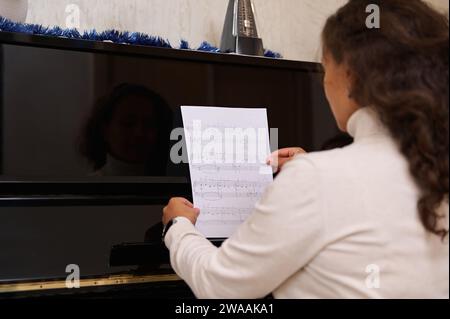 Vista posteriore di una pianista femminile con note di composizione musicale classica, seduta al vecchio pianoforte nero, pronta a suonare una melodia. Arte, cultura e enterta Foto Stock