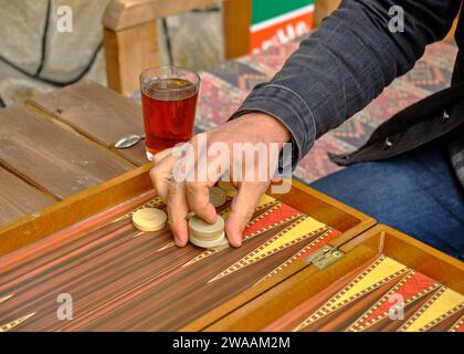 Uomo che raccoglie quattro pezzi dal gioco da tavolo del backgammon in un gioco all'aperto Foto Stock