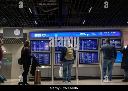 Una folla di persone a tarda notte davanti alla bacheca informativa all'aeroporto, alla ricerca di informazioni sui voli di coincidenza dopo l'imbarco nella zona di transito Foto Stock