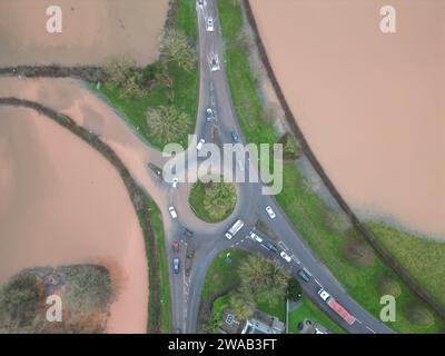 Hereford, Herefordshire, Regno Unito – mercoledì 3 gennaio 2024 – tempo nel Regno Unito – Vista aerea dei campi allagati e delle strade alla periferia di Hereford lungo la strada A4103 per Worcester. Questa inondazione proviene dal fiume Lugg con la strada locale per Sutton St Nicholas chiusa a questa rotatoria a causa delle inondazioni. Foto Steven May / Alamy Live News Foto Stock