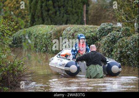 Worcester, 3 gennaio 2024 - Jack, di 7 anni e mezzo, viene trasportato in barca alla sua casa nel borgo inglese di Severn Stoke, completamente tagliato dalle inondazioni dopo che il fiume Severn ha fatto scoppiare le sue rive a causa delle continue piogge della tempesta Henk. Il pub Rose and Crown potrebbe essere visto pompare acqua mentre combatteva per rimanere asciutto con le loro difese fatte in casa contro le inondazioni. - Credito: Stop Press Media/Alamy Live News Foto Stock